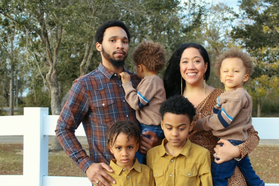 Family with four kids standing next to a white fence